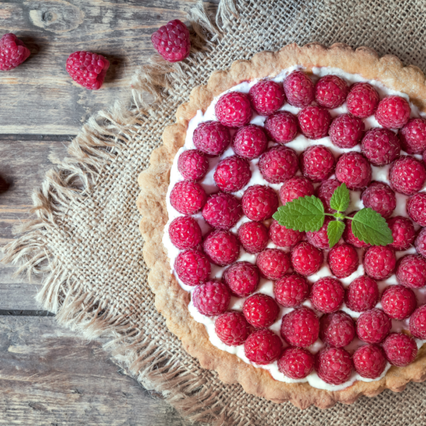 Raspberry Tart on a burlap sack table cloth on a wooden table, garnished with a lemon sprig