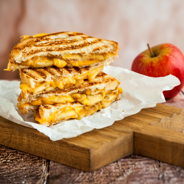 Grilled cheese sandwhich halves on a cutting board next to red apples